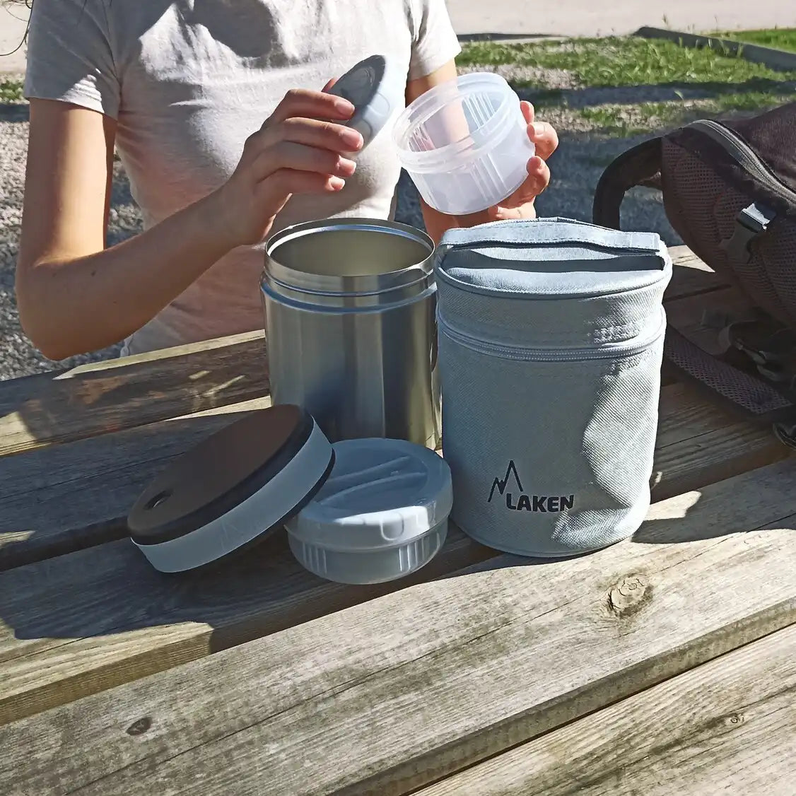 Mujer abriendo el termo para alimentos LAKEN en una mesa de camping